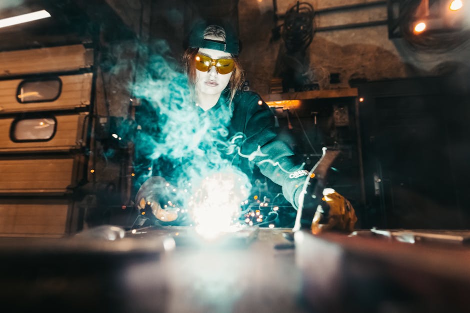 A female welder working with sparks flying, wearing protective gear in an industrial workshop.